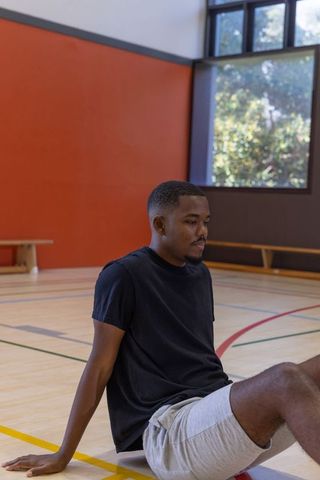 African american man sitting on indoor gym court leaning back in casual athletic wear