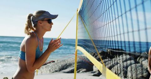 Female Beach Volleyball Player Serving on Sunny Oceanfront Court Near Waves