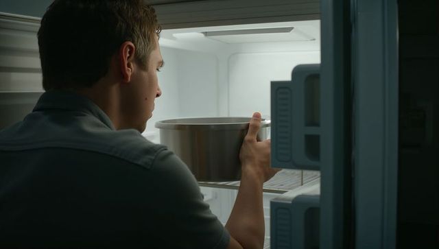 Man placing stainless-steel pot into open refrigerator illuminated interior back view kitchen