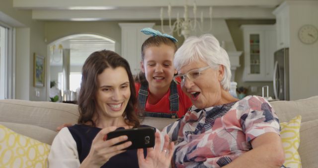 Family spending quality time together in living room. Grandmother, mother, and child happily looking at smartphone. Ideal for themes like family bonding, technology, intergenerational relationships, home life.