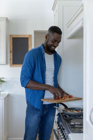 Man slicing cherry tomatoes for cooking in modern kitchen