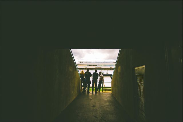 Group of people standing at tunnel entrance, observing stadium. Perfect for depicting anticipation before sports events, stadium architecture, or crowd dynamics during sports games.