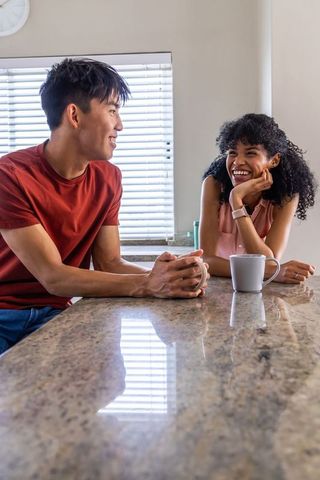 Smiling interracial couple chatting over coffee at kitchen counter with smartwatch
