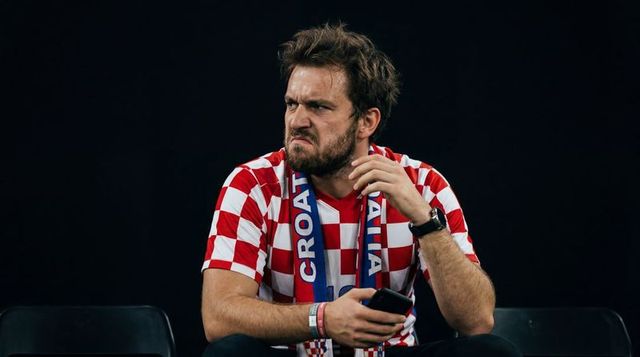Frustrated bearded croatian fan checking phone in stands wearing checkered jersey
