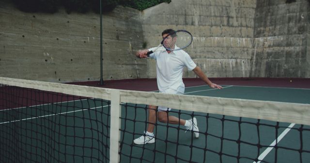 Man focused on returning a tennis serve while wearing white sports attire. The image captures the intensity and athleticism of the game. Ideal for use in sports-related articles, advertisements for sports equipment, fitness and health campaigns, and recreational activity promotions.