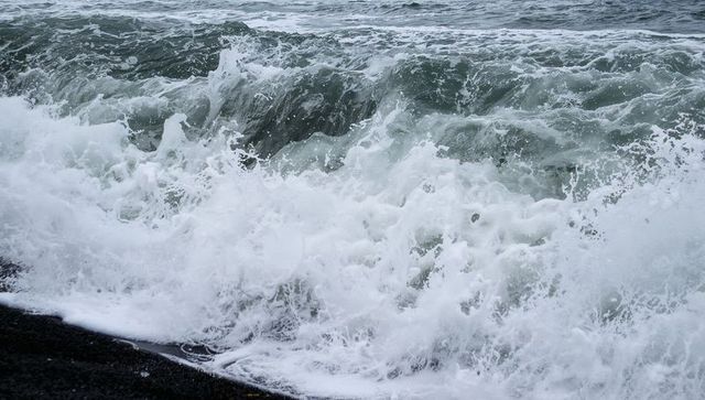 Crashing ocean wave breaking on black shore with powerful white foam and turbulent surf