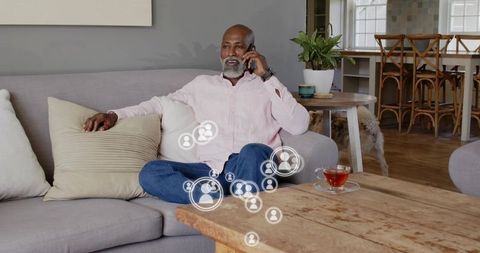 Mature man chatting on smartphone in cozy sunlit living room with social network icons