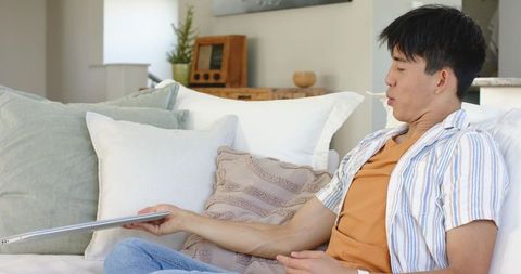 Young asian man reclining on sofa holding slim laptop, relaxed minimalist home lifestyle