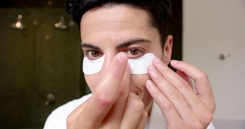 Man applying under eye mask in modern bathroom for skincare routine