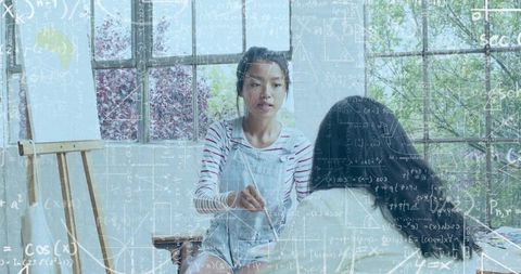 Asian art instructor demonstrating painting lesson in sunlit studio with math overlay