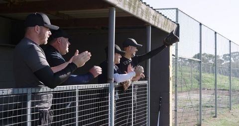 Veteran baseball team cheering and reaching with glove from dugout during sunny game play