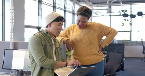 Asian man and African American woman collaborating on laptop in modern open office