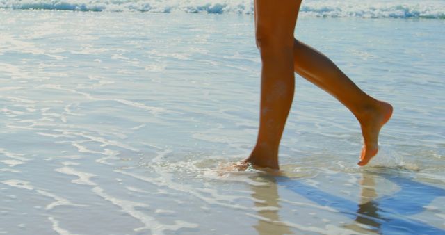This image portrays a woman walking along a sandy shoreline with tranquil ocean waves. Perfect for travel advertisements, beach destination promotions, health and wellness campaigns, and lifestyle content focusing on relaxation and leisure activities.