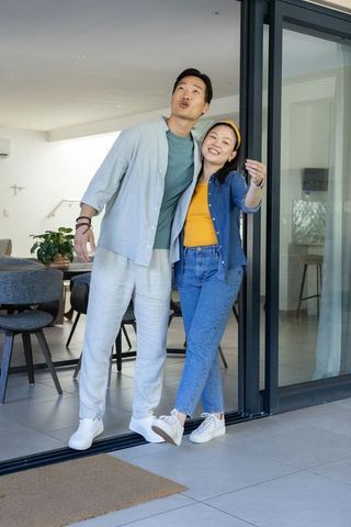 Asian couple moving into new home standing at sliding glass door pointing to doormat