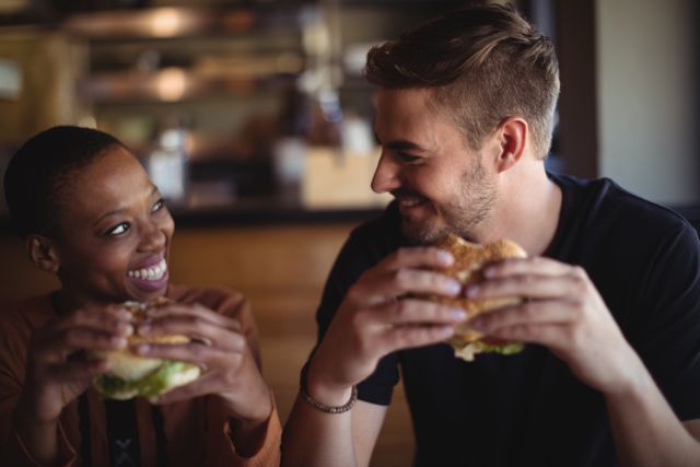Happy couple enjoying burgers together in a relaxed restaurant environment. Ideal for use in advertisements related to dining experiences, restaurant promotions, fast food marketing, and social bonding activities.