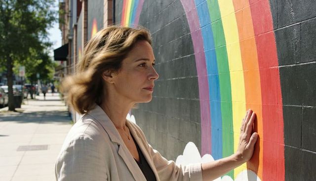 Woman touching rainbow mural on urban brick wall reflecting during sunny street walk