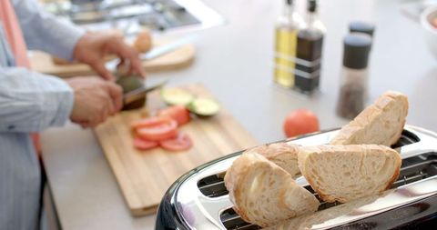 Man Slicing Avocado and Tomato with Toaster in Home Kitchen