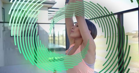 Young woman stretching and raising arms on glass balcony with green circular overlay