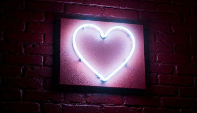 Blue-white neon heart sign casting pink glow on red brick wall