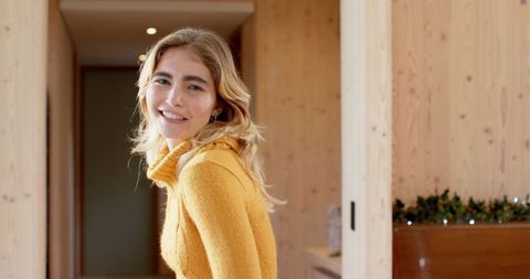 Smiling woman in cozy sweater in warmly lit rustic hallway