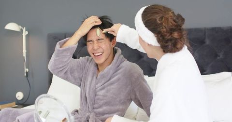 Diverse couple sharing playful at-home skincare moment with facial roller and robes
