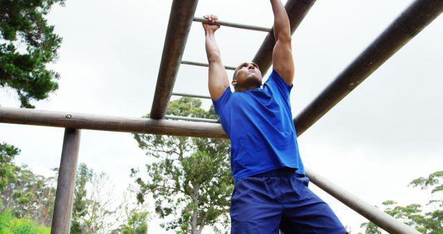 A young African American male is engaged in a pull-up exercise on outdoor fitness equipment, with copy space. His workout demonstrates strength training and a commitment to physical health.