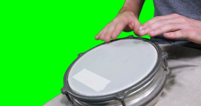 Mid section of drummer playing drum against green screen