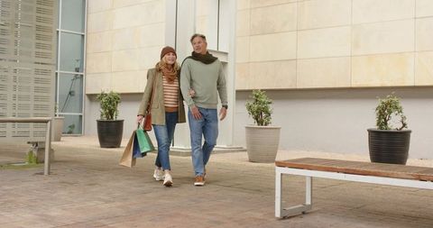 Mature couple walking arm-in-arm after shopping in urban plaza wearing cozy fall layers