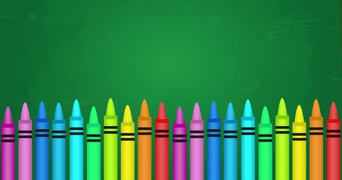 Colorful wax crayons lined up on green chalkboard background