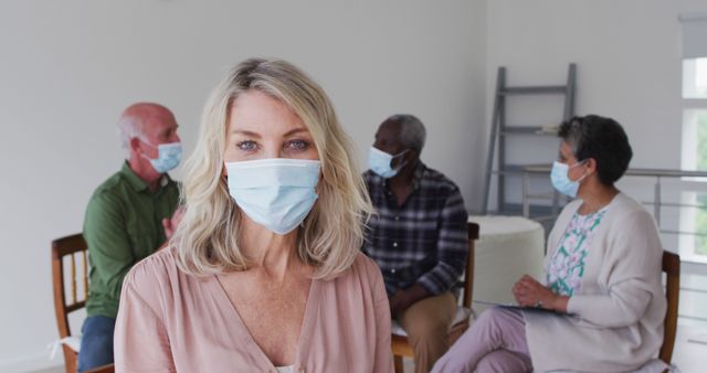 Group of mature individuals from diverse backgrounds engaged in conversation while wearing face masks. Ideal for illustrating health awareness, social distancing, community support, and safety measures in indoor group settings.