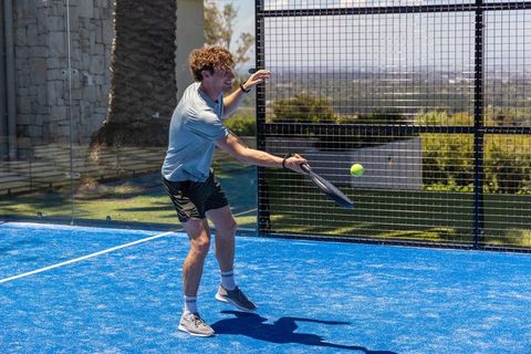 Athlete playing padel tennis on blue court hitting ball mid-swing in sunny outdoor match