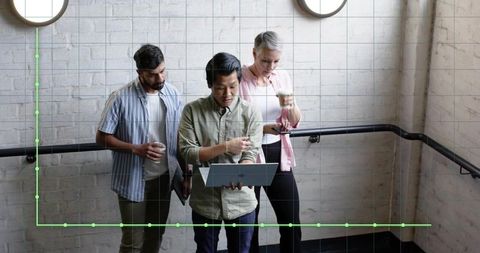Diverse Professionals Collaborating Over Laptop in Office Stairwell