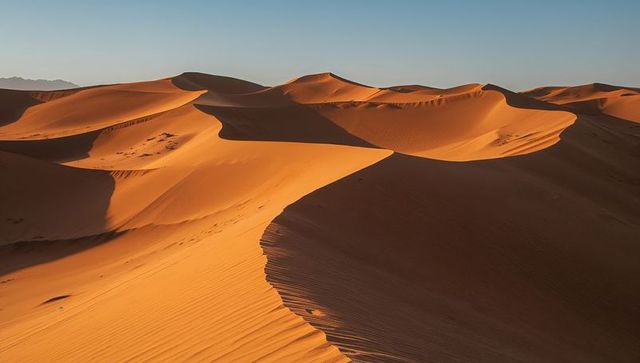 Sunlit sand dunes sculpting curved ridges and rippled texture in desert landscape