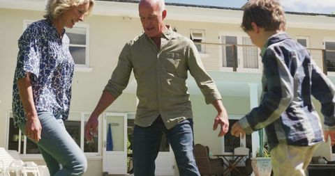 Happy Senior Couple Playing Football with Grandson in Backyard