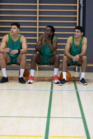 Diverse basketball players in gym sitting on bench