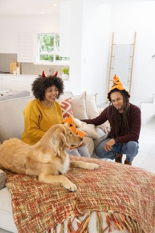 Cozy halloween at home: african american couple petting golden retriever, pumpkin fun