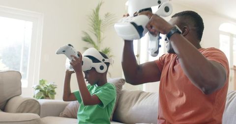 Father and son putting on VR headsets on sofa enjoying family tech bonding in sunlit room