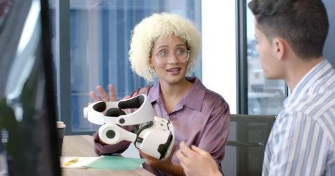 Creative professional presenting white vr headset to colleague in modern office meeting