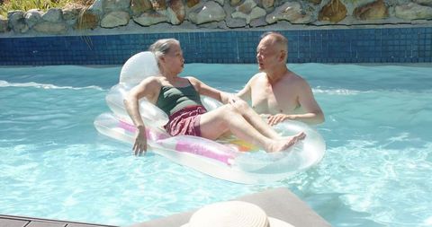 Senior couple lounging on inflatable float in sunny backyard pool