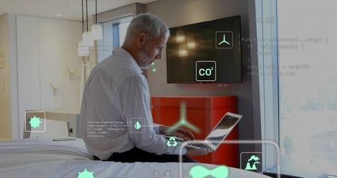 Senior man working remotely on laptop in hotel room with ar environmental dashboard