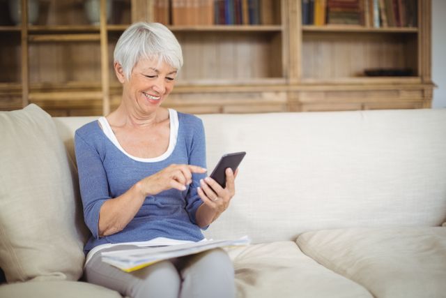 Smiling senior woman using mobile phone in living room at home