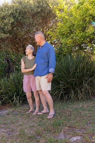 Senior asian couple laughing and embracing in garden sunlight, casual summer lifestyle