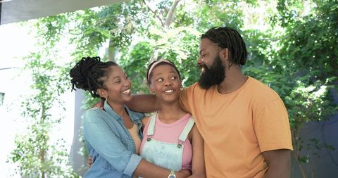 African american parents hugging teenage daughter on porch smiling in sunlit garden