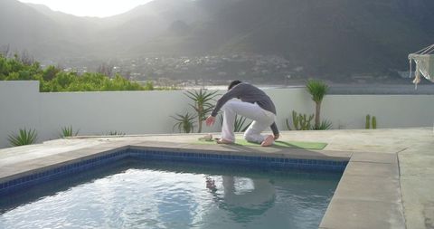 Poolside morning yoga stretching by indian man on mat beside mountain view pool