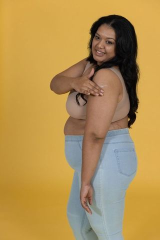 Plus-size woman applying moisturizer on arm smiling against bright yellow background