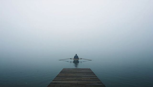 Solitary rower rowing into misty dawn from wooden dock, minimalist calm lake landscape