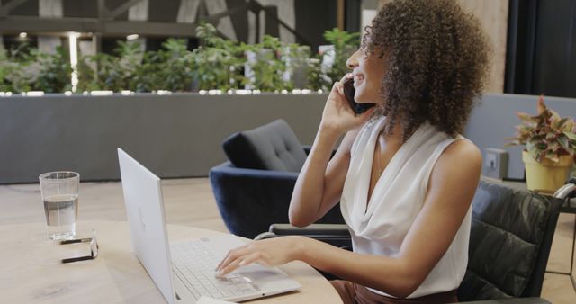 Businesswoman with curly hair talking on phone and working on laptop in modern office - Download Free Stock Images Pikwizard.com