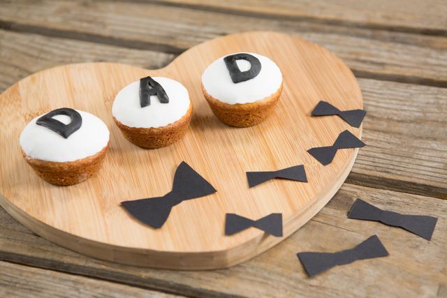 Cupcakes with 'DAD' text and black bow ties on a wooden table. Ideal for Father's Day celebrations, family gatherings, and dessert-themed events. Perfect for social media posts, greeting cards, and festive decorations.