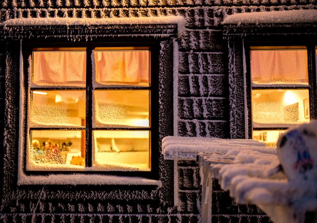 Warm, glowing windows contrast against a snowy cabin exterior on a winter night, evoking a sense of coziness and serenity. Great for advertising mountain retreats, winter holidays, and seasonal greeting cards.