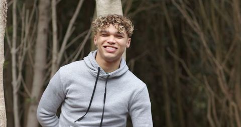 Young man in gray hoodie smiling in peaceful woodland